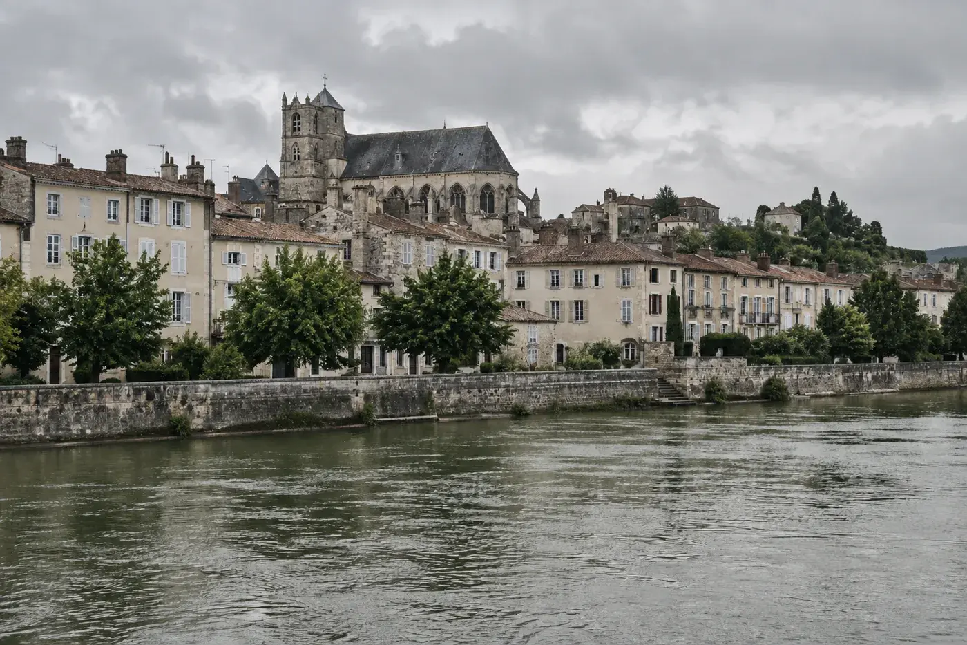 Maisons anciennes aux toits de tuiles et grande église gothique en pierre au bord de la Seine, sous un ciel couvert